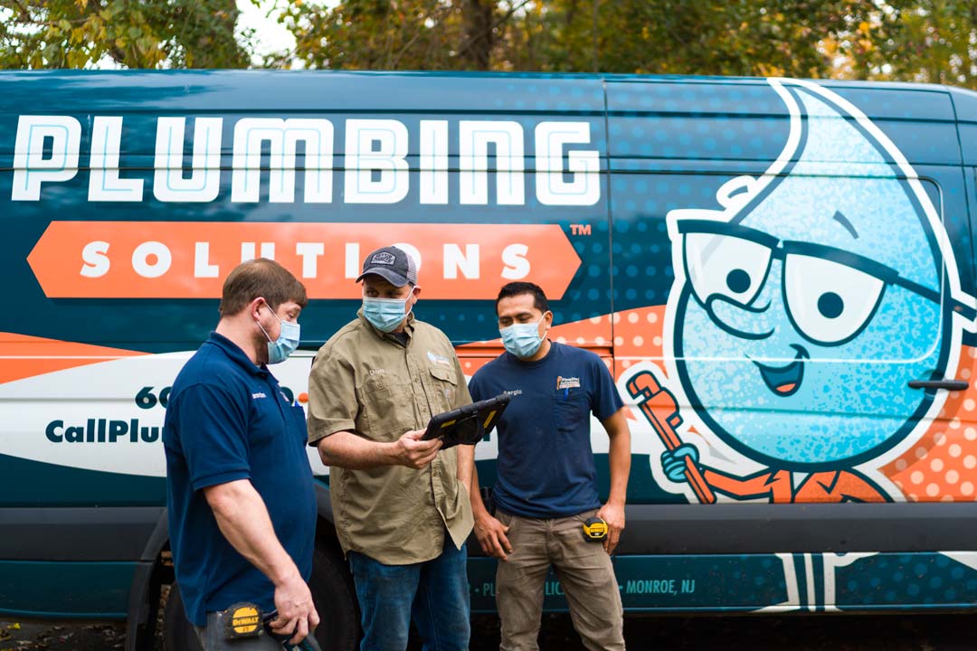 Plumbing Solutions Inc., crew members and master plumber Don Meier, standing infront of branded PSI plumbing truck examining a tablet with project specifications