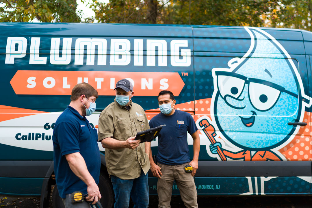 Plumbing Solutions Inc - Owner and Master Plumber, Don Meier discusses a job with the crew while looking at a tablet. Standing in front of a Plumbing Solutions Inc. truck.