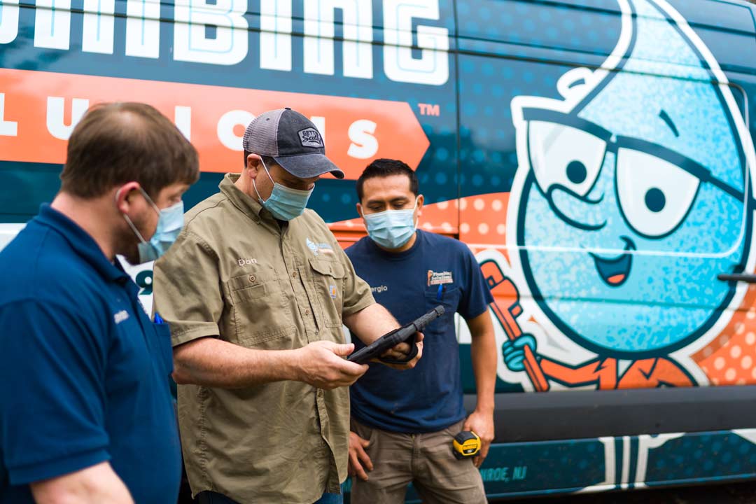 Plumbing Solutions Inc - Owner and Master Plumber, Don Meier discusses a job with the crew, who are all wearing masks, while looking at a tablet. Standing in front of a Plumbing Solutions Inc. truck.