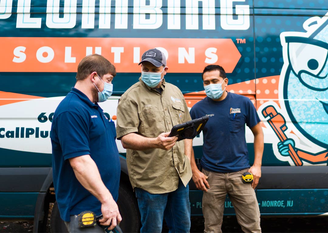 Don Meier and Technicians Discussing a project looking at a tablet in front of Plumbing Solutions truck