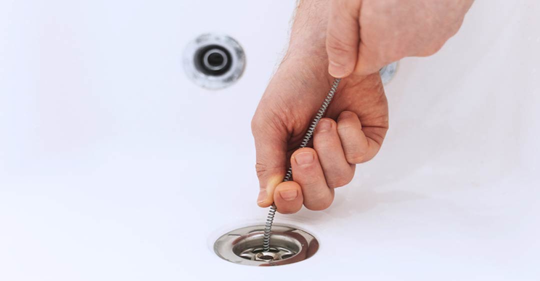 Plumbing Solutions - two hands cleaning a drain with a plumbing snake
