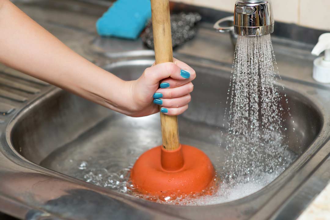 Picture of a hand using a plunger in a sink with water running