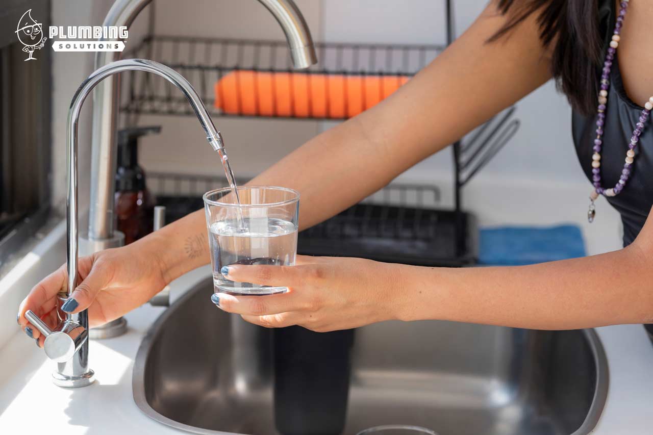 Plumbing Solutions Inc. - a woman filling up a glass of clean water from a sink